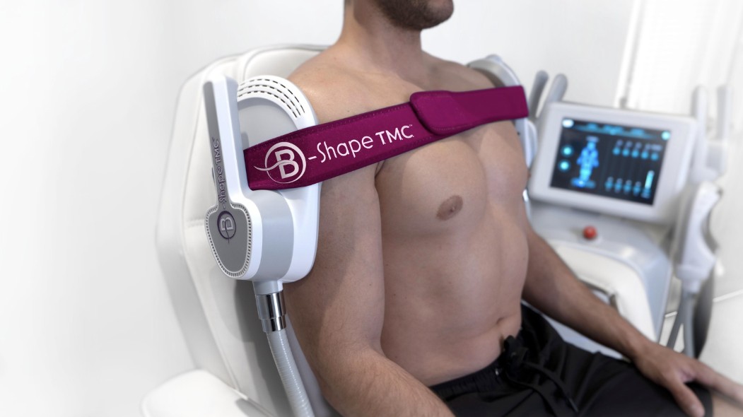 Un client assis en séance B-Shape, un applicateur maintenu sur les épaules par une sangle violette